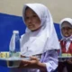 Dua murid membawa nampan menu MBG di sekolah dasar Sumedang, menu bahan mentah MBG jadi sorotan.